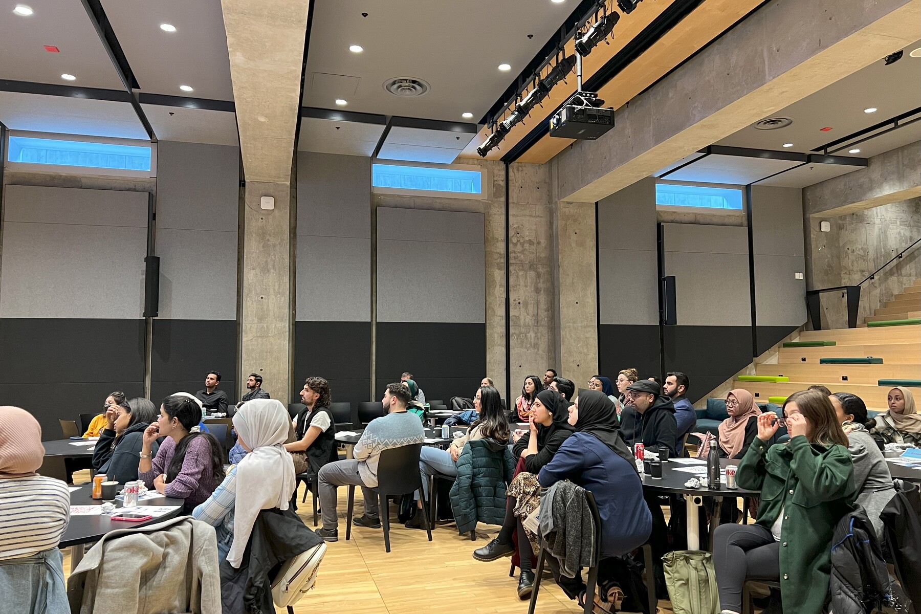 People in a large room sitting around round tables listening to a presentation