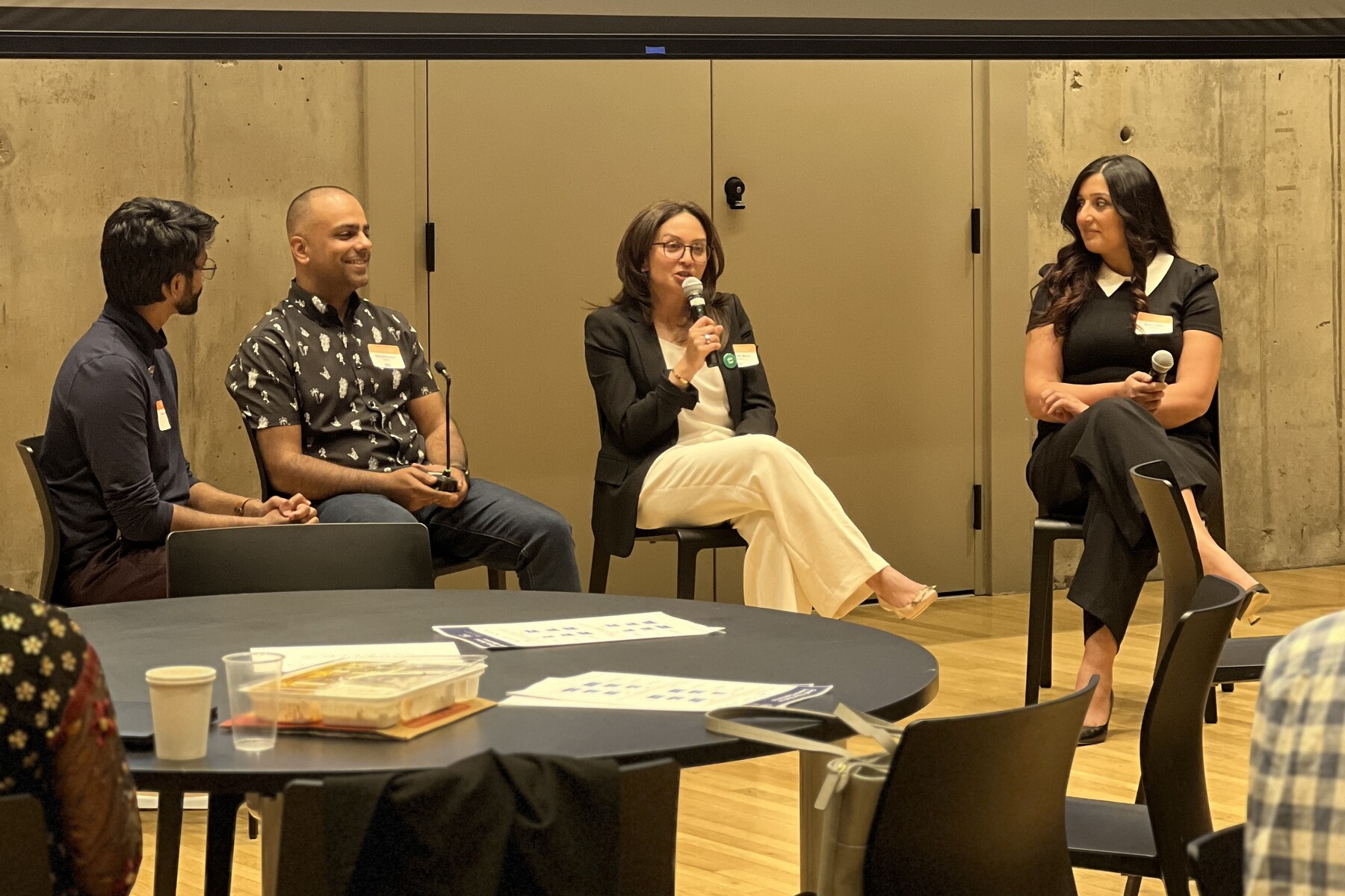Four people sitting in chairs in a panel formation. The person second from the right holds a microphone.