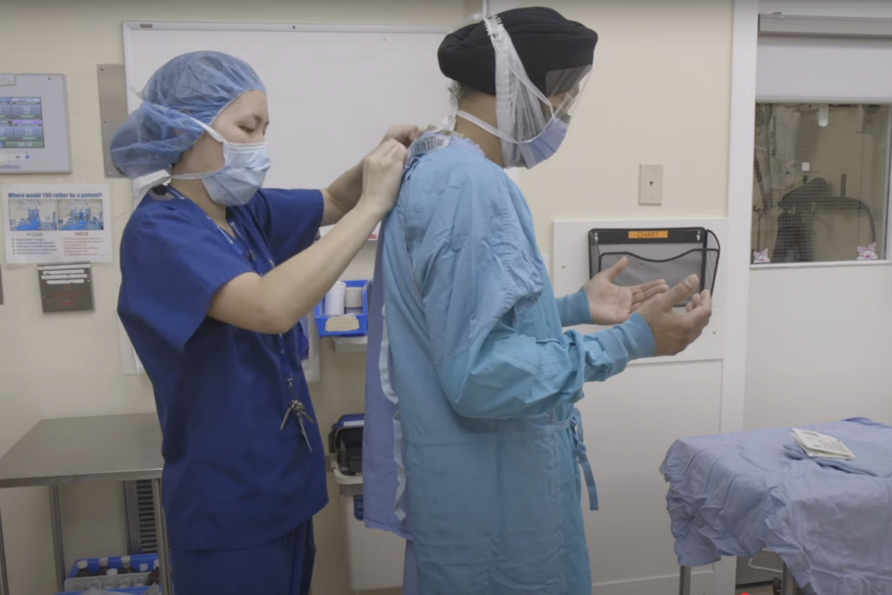 A nurse helps a man wearing a turban put on a surgical gown and mask
