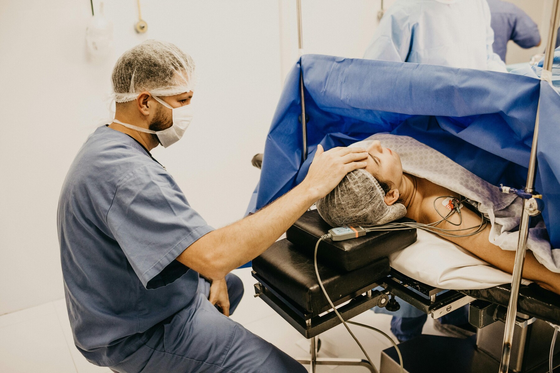 An anesthesiologist wearing scrubs touching the head of a patient lying in an operating room
