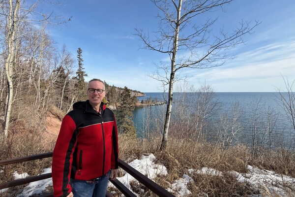 Jason Shack stands on a trail in northern Ontario in the winter. He is wearing a red jacket. 