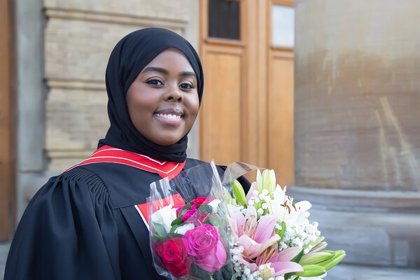 Portrait of Samira Omar in convocation robe and holding a bouquet of flowers