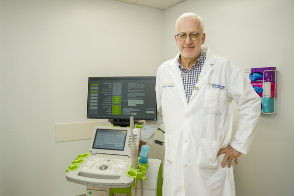 Laurence Klutz wearing a white doctor's coat standing with an ultrasound machine