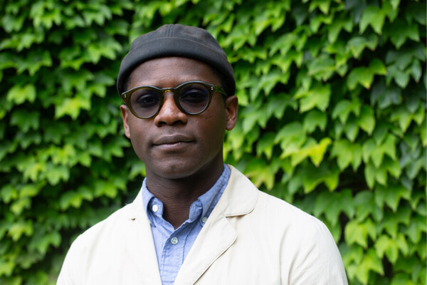 Michael Zarathus-Cook wears a black beanie, a white cardigan and black sunglasses