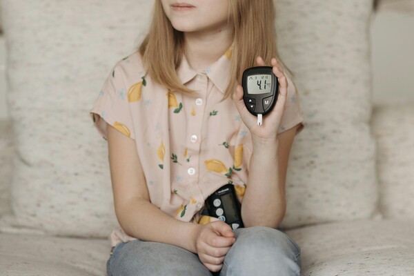 Little girl sitting on a sofa and showing her glucometer