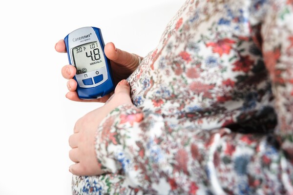 A pregnant person wearing a flowered shirt and holding a glucose monitor