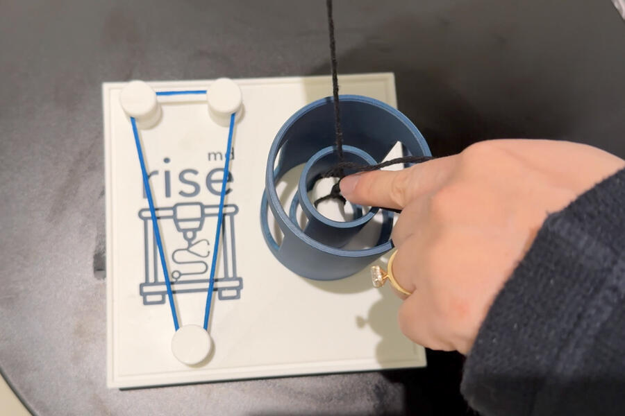 A hand holds string on a knot-tying board