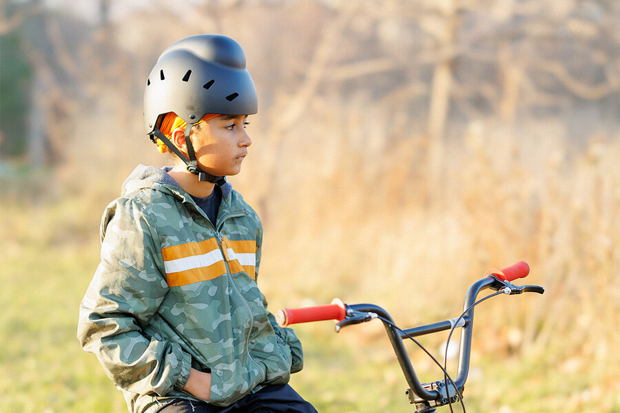 A child sits on a bicycle and wears a helmet designed to fit over a patka, or cloth head covering. 