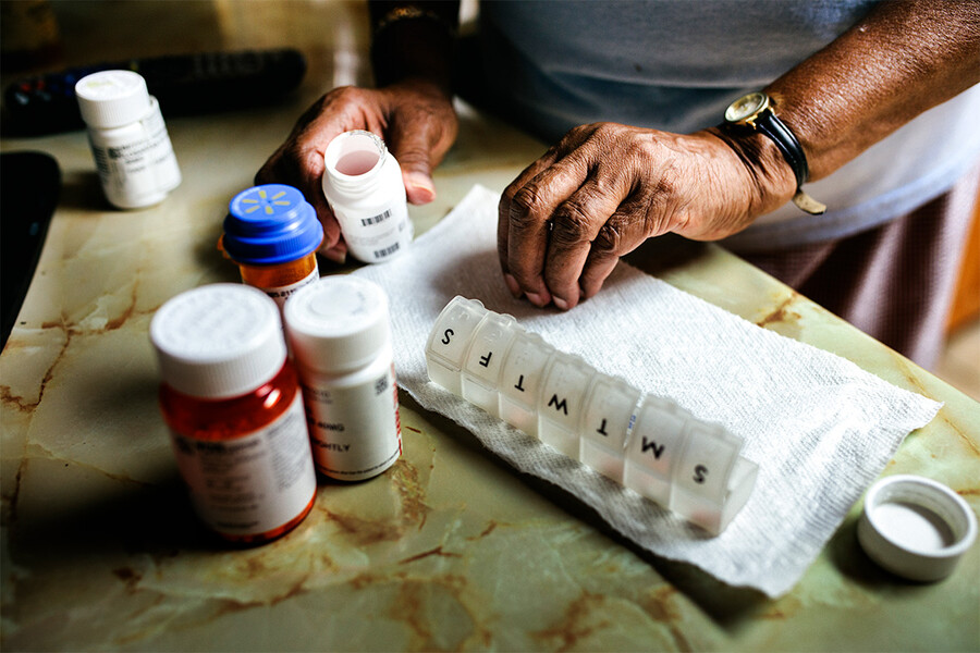 An unidentifiable person is shown sorting medication into a pill organizer