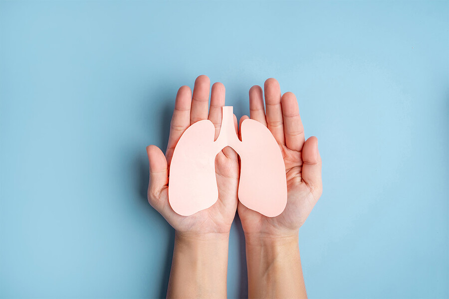 A pair of hands holds a paper cut out in the shape of a pair of lungs.