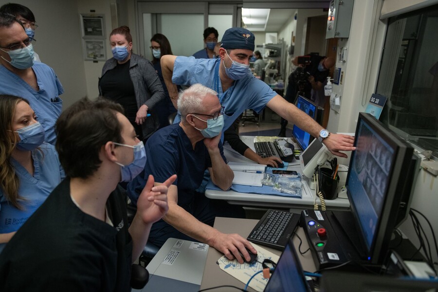 Nir Lipsman and James Rutka look at a computer screen while surrounded by colleagues