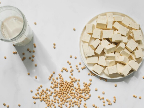 A glass of soy milk, a bowl of cubed tofu and some soy beans.