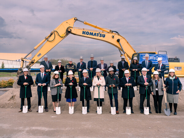 Stakeholders wearing hardhats and holding shovels stand in front of a digger at the SAMIH groundbreaking