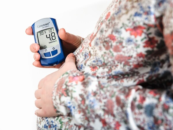 A pregnant person wearing a flowered shirt and holding a glucose monitor