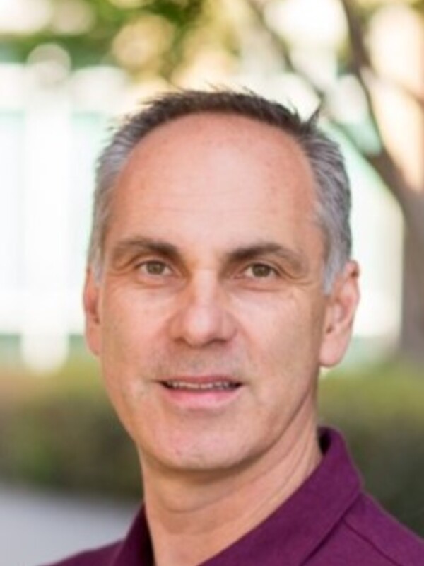 A man in a purple collared shirt with short hair smiles for the camera