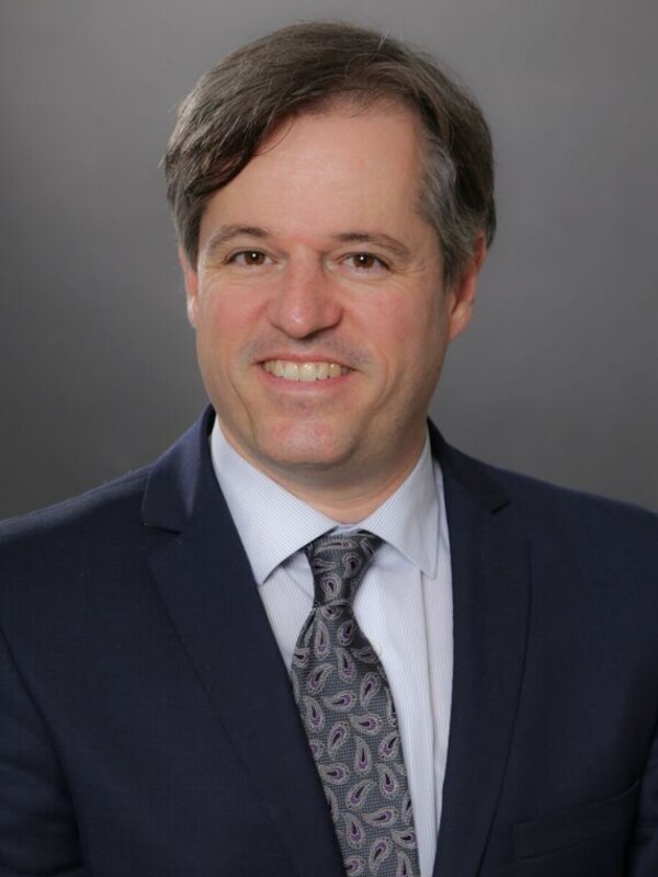 Dr Piguet smiles for the camera, he is wearing a dark blue suit.