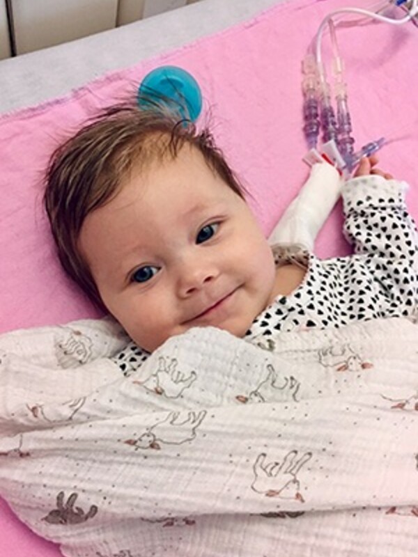 A baby, awake under a light blanket in a hospital