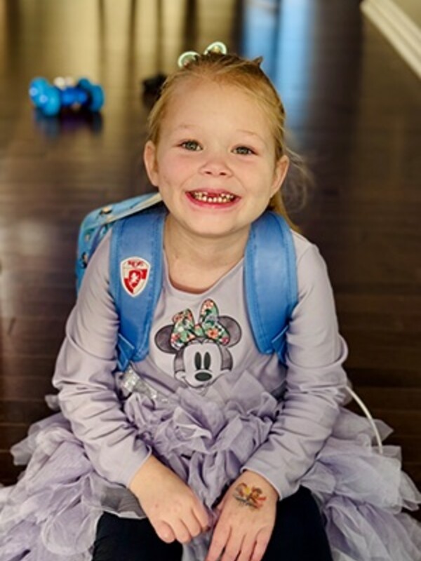 A smiling child sits on a floor wearing a backpack