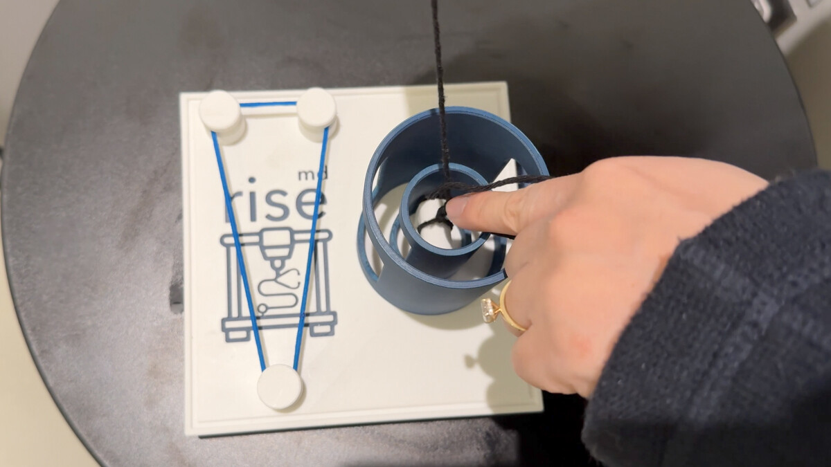 A hand holds string on a knot-tying board