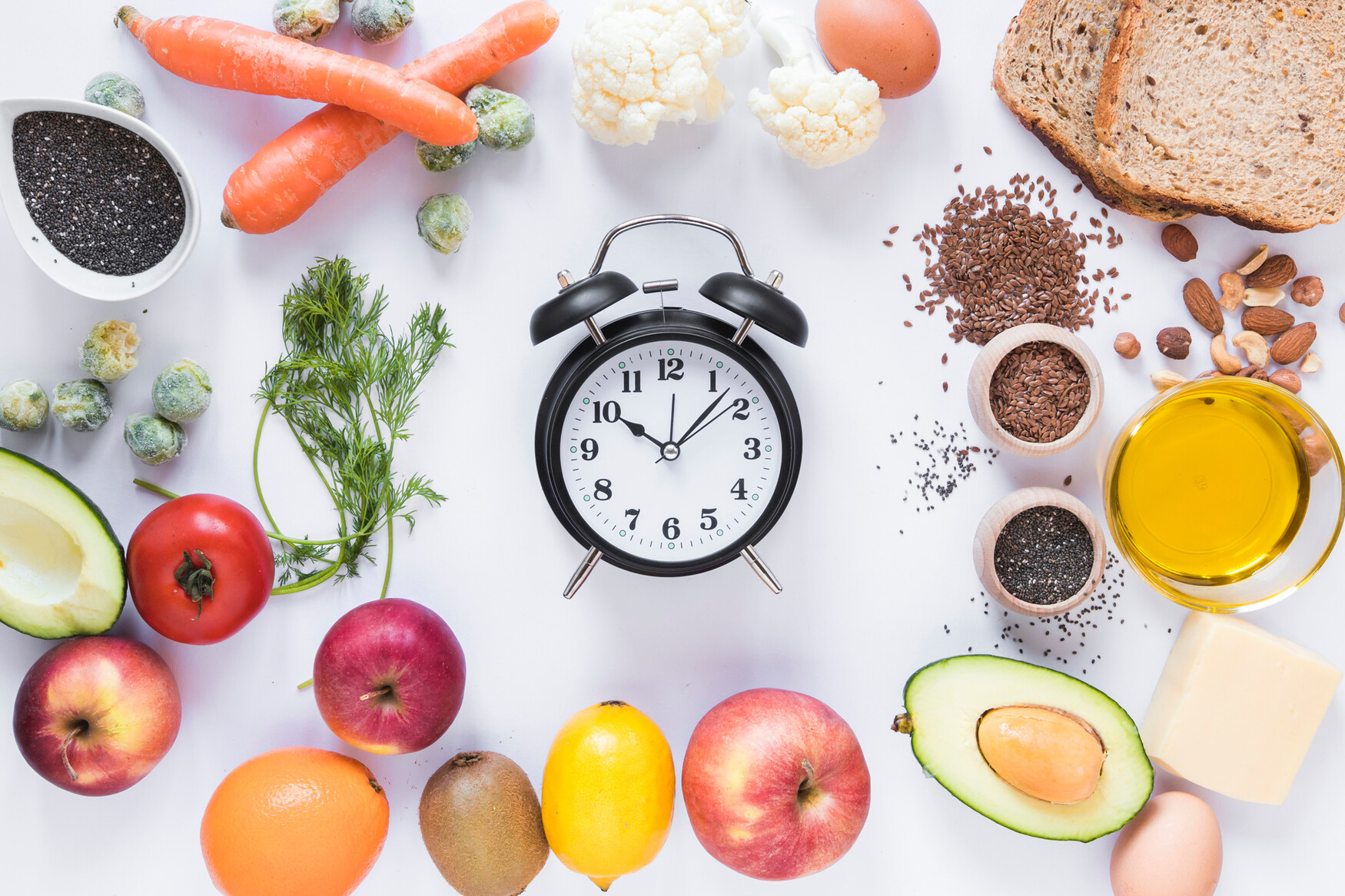 An alarm clock surrounded by a variety of fresh fruits, vegetables, grains and other ingredients