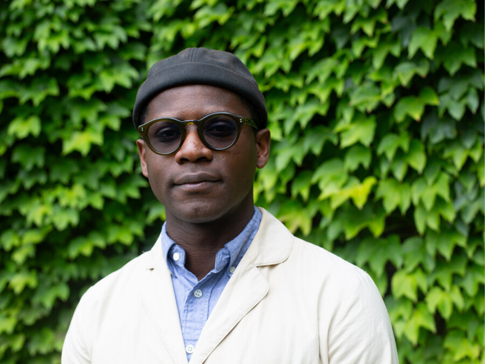 Michael Zarathus-Cook wears a black beanie, a white cardigan and black sunglasses