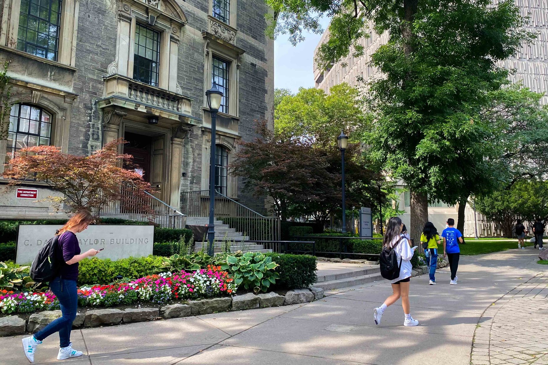 People walk on the path in front of the Naylor Building on the U of T St. George Campus on a sunny, warm day.