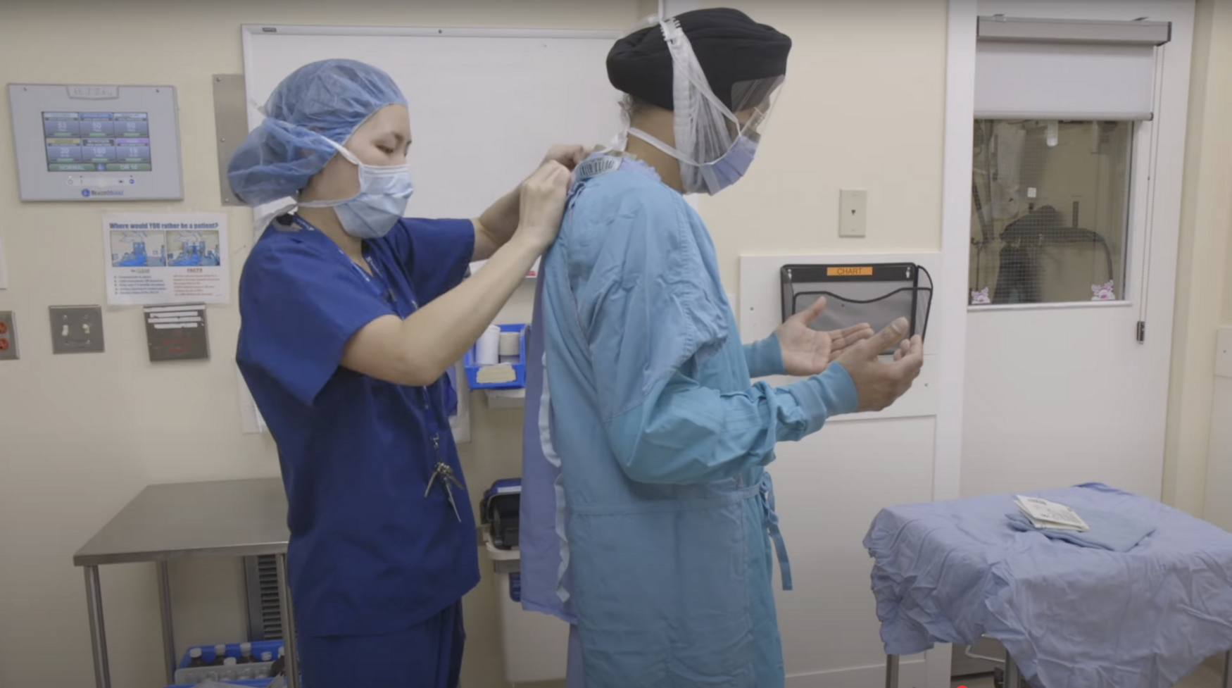 A nurse helps a man wearing a turban put on a surgical gown and mask