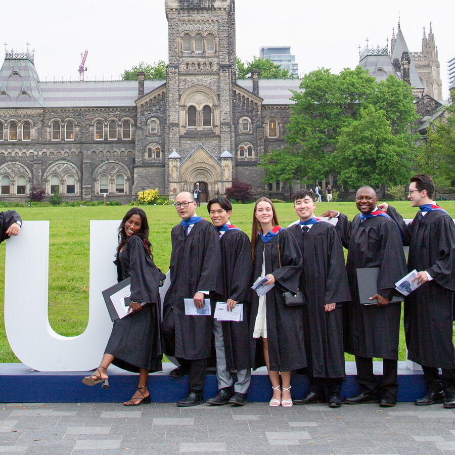 A group of graduates poses with a U of T sign on King's College Circle
